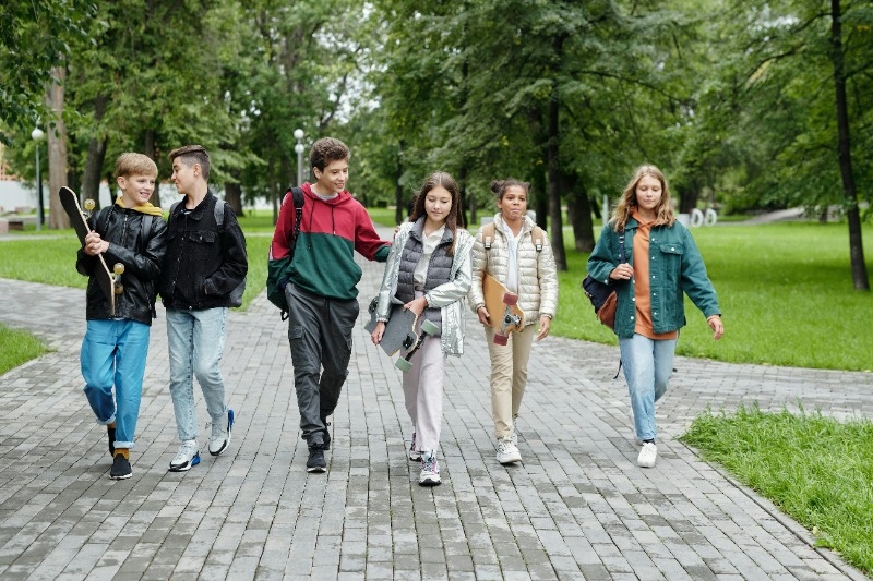 Pre-teens walking in a line. Some carrying skateboards and others have bookbags on the backs