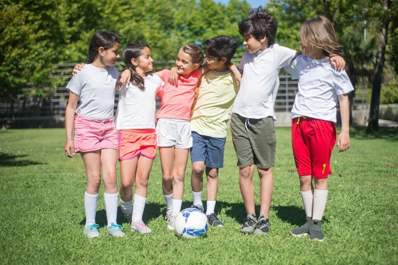 a group of boys and girls standing in a line with their arms on each others shoulders with a soccer balls at their feet