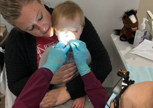 toddler receiving dental services while in the lap of his childcare provider