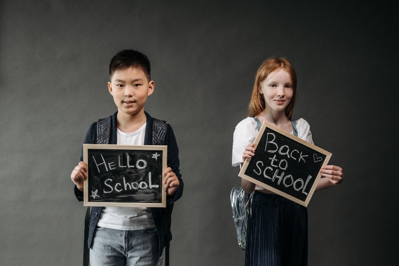 Two children holding small chalkboards that say Hello School and the other one says Back to school